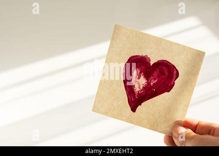 A drawn heart on a paper sticker. Heart on the paper in his hand. A symbol of love and unity. Natural soft light with shadows. Creative layout of a Va Stock Photo