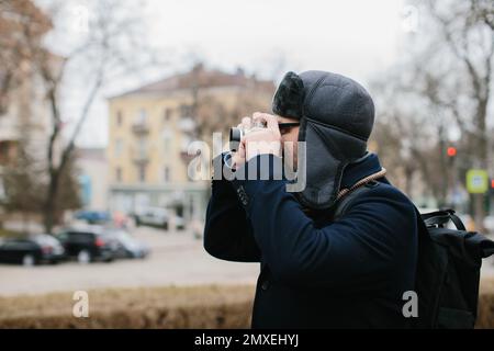 A senior tourist takes pictures of the winter city on his film camera. Travel and hobby concept. Stock Photo