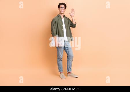 Full body size cadre of young friendly guy worker copywriter hold netbook palm hello office employee wear glasses isolated on beige color background Stock Photo