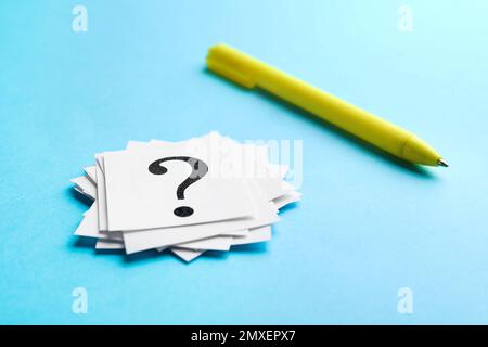 Heap of paper notes with question marks and pen on light blue background, closeup Stock Photo