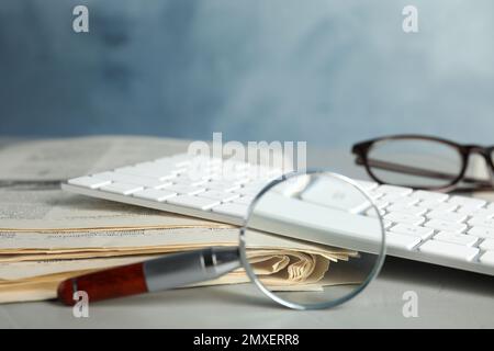 Magnifying glass, keyboard and stack of newspapers on grey table, space for text. Job search concept Stock Photo