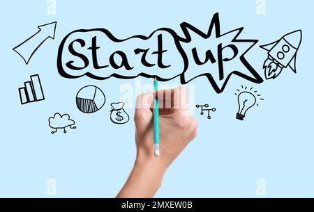 Woman drawing different icons and word STARTUP with pencil on light blue background, closeup Stock Photo
