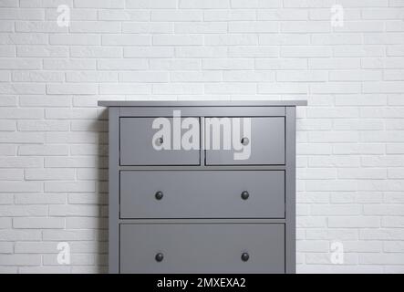 Grey chest of drawers near white brick wall indoors Stock Photo