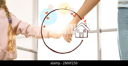 Mother holding hands with child and illustration of house indoors, closeup. Adoption concept Stock Photo