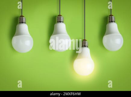 Idea concept. Glowing light bulb among others on green background Stock Photo