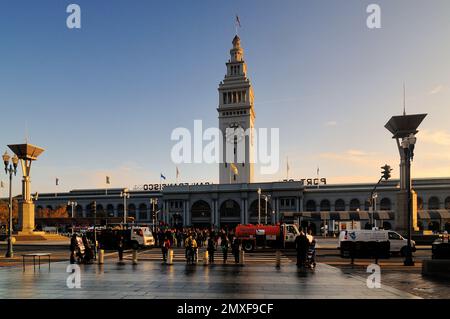 The iconic San Francisco Ferry Building with its clock tower at sunset. Crowds, street lamps, and reflections create a scenic view at this historic wa Stock Photo