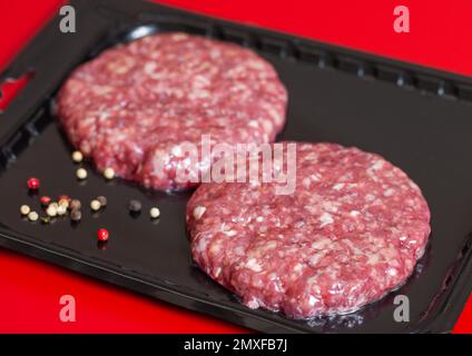 Raw minced beef burgers in plastick vacuum tray on red. Stock Photo
