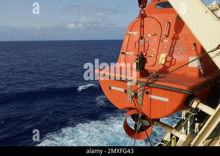 View on the aft part of orange colour lifeboat with reflective tape stickers secured with davits and safety hooks on the container cargo vessel. Stock Photo