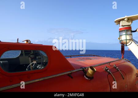 Close view on cabin of the orange colour life boat with reflective tape stickers secured with davits and safety hooks Stock Photo