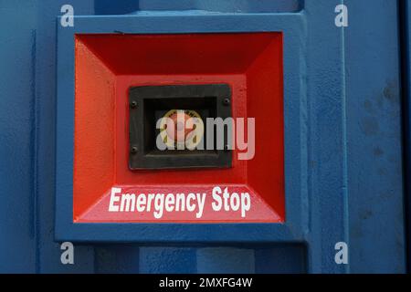 Red Emergency stop button placed on the wall of blue container of electric power pack. Stock Photo