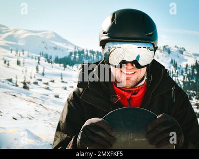 Close up portrait caucasian man with the reflection of snowed mountains, white slope and ski resort. A mountain range reflected in the ski mask. Portr Stock Photo