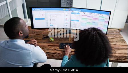 Young Businesspeople Analyzing Gantt Chart And Calendar On Computer In Office Stock Photo