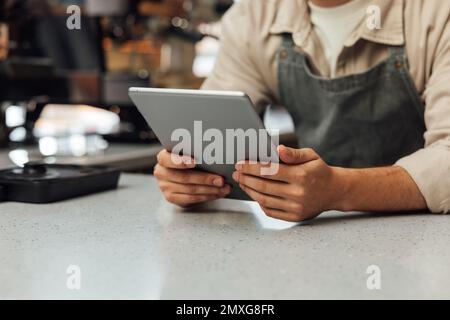 Close-up of hands holding a digital tablet. Unrecognizable bartender in an apron holding a portable computer at the counter. Stock Photo