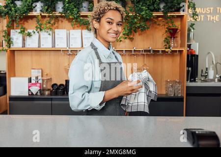 Smiling male bartender wiping a glass and looking away. Barista in