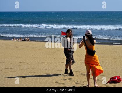 Two woman on Maspalomas sandy beach when its windy, one taking photos of the other, Gran Canaria Stock Photo