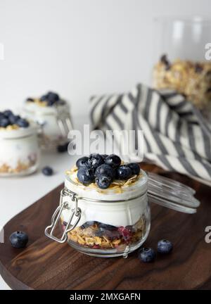 Breakfast oatmeal with fruit in a glass jar made from greek yogurt and granola topped with fresh blueberries on striped cloth with honey spoon, health Stock Photo
