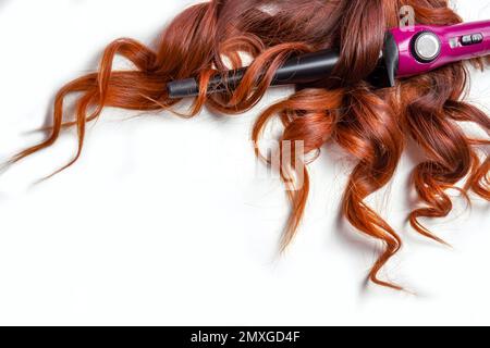 long red curly hair on white isolated background with curling iron . Stock Photo