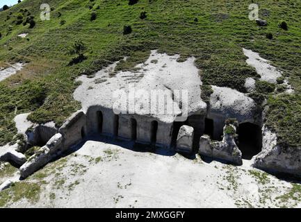 A high-angle view of stone caves at the Tepe Kermen under a hill in Crimea Stock Photo