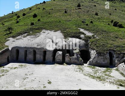 A high-angle view of stone caves at the Tepe Kermen under a hill in Crimea Stock Photo