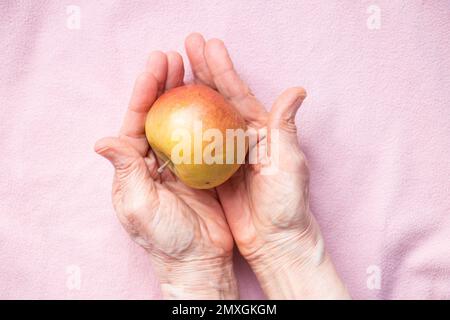 apple in the hands of grandmother on a pink background close up Stock Photo