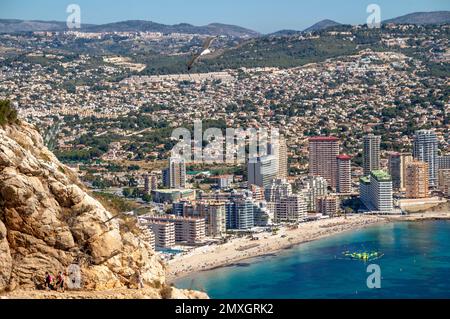 beach with buildings and seagulls flying and people hiking. Rock of penon by Ifach. Mediterranean coast landscape in the city of Calpe. Coastal city l Stock Photo