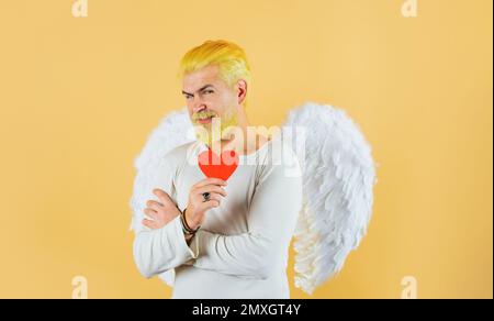 Happy Valentines Day. Cupid with red paper heart. Bearded man in angel wings with Valentine card. Stock Photo