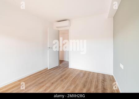 Bright spacious bedroom with parquet flooring. An open door from the room leading to a corridor with other rooms. Air conditioning above the door Stock Photo