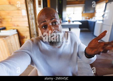 Confused african american bald senior man shrugging his shoulders in log cabin Stock Photo