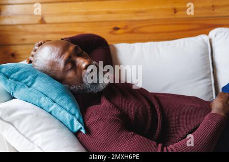African american bald senior man sleeping on couch in log cabin Stock Photo