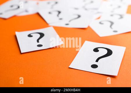 Paper notes with question marks on orange background, closeup Stock Photo