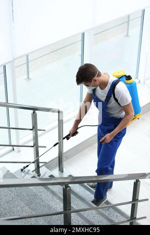 Pest control worker spraying pesticide near stairs indoors Stock Photo