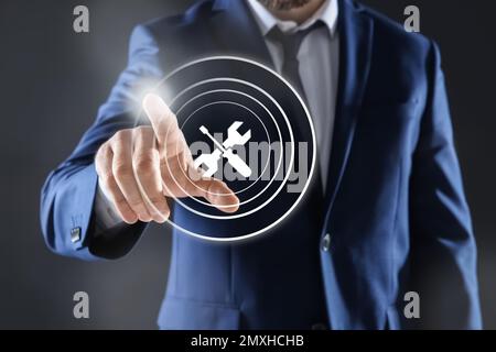 Man touching icon on virtual screen against dark background, closeup. Technical support Stock Photo