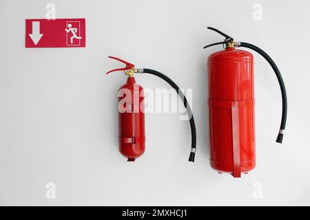 Fire extinguishers and emergency exit sign on white wall Stock Photo