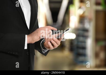 Wholesale trading. Man using WMS app on smartphone at warehouse, closeup Stock Photo