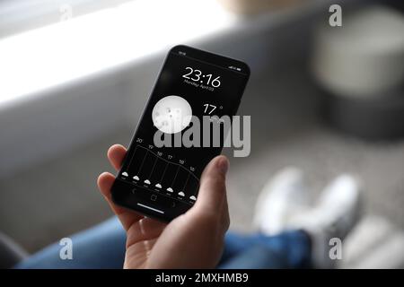 Man using weather forecast app on smartphone indoors, closeup Stock Photo