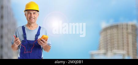 Mature electrician with multimeter against cityscape, space for text. Banner design Stock Photo