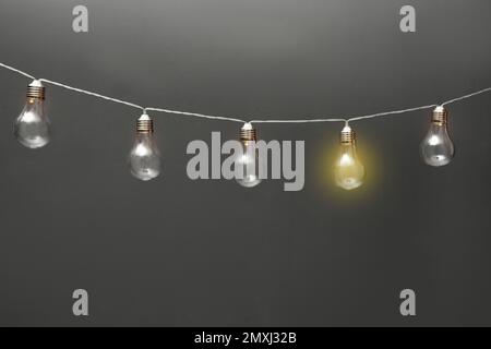 Idea concept. Garland of light bulbs with one glowing on grey background Stock Photo