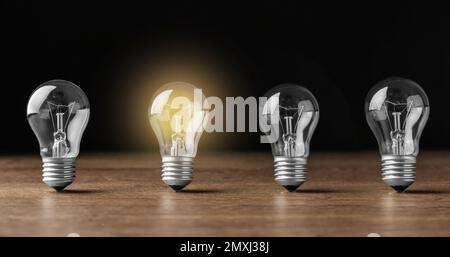 Idea concept. Glowing light bulb among others on wooden table against black background, banner design Stock Photo