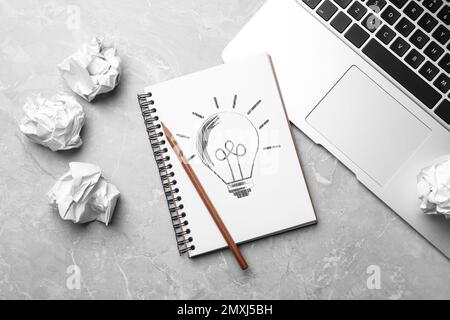 Notebook with drawn lamp and crumpled paper on grey table, flat lay. New idea concept Stock Photo