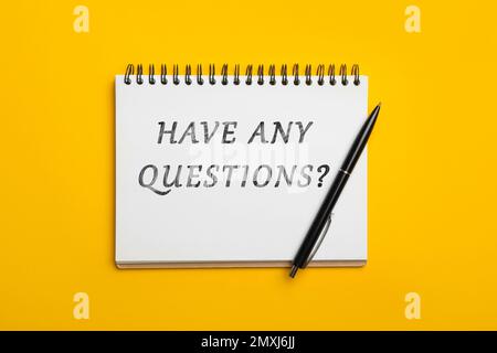 Open notebook with phrase HAVE ANY QUESTIONS and pen on yellow background, top view Stock Photo