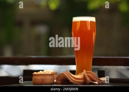Glass of tasty beer served with snacks on table outdoors, space for text Stock Photo