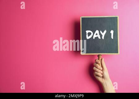 Starting new life. Woman holding blackboard with text Day 1 on pink background, closeup. Space for text Stock Photo