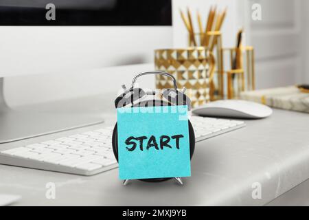 New job. Sticker with word Start on alarm clock near computer in modern office Stock Photo