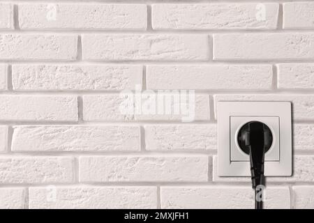 Brick wall with power socket and inserted plug, space for text ...