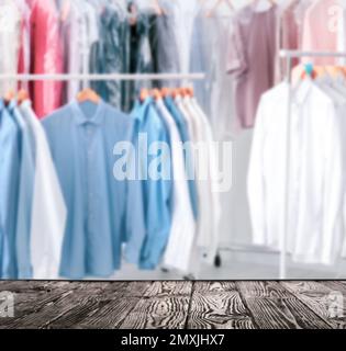 Empty black wooden surface and clean clothes on hangers in dry-cleaning, space for text Stock Photo