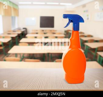 Protective measures during Coronavirus pandemic. Bottle of disinfectant on table against classroom, space for text Stock Photo