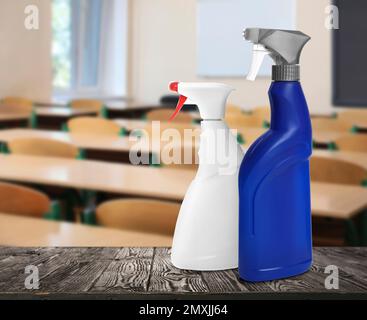 Protective measures during Coronavirus pandemic. Bottles of disinfectant on table against classroom, space for text Stock Photo