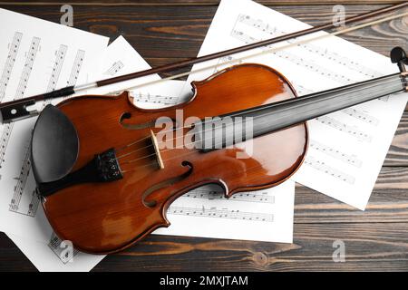 Beautiful violin, bow and note sheets on wooden table, flat lay Stock Photo