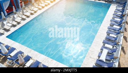 Lounge chairs with umbrellas near swimming pool on sunny day Stock Photo