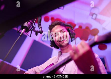 Happy man, musician or guitar in neon studio, recording production or performance for radio, label or low angle concert. Guitarist, artist or singer Stock Photo
